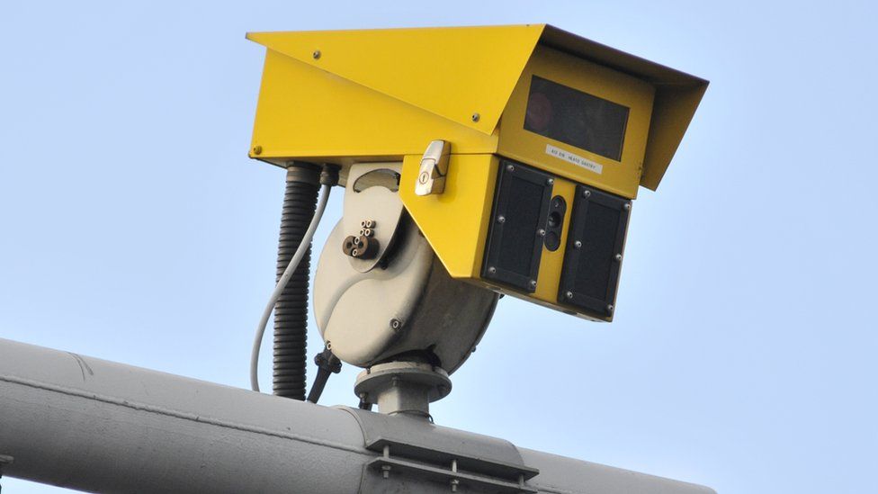 A yellow speed camera is mounted on a pole in this close-up shot