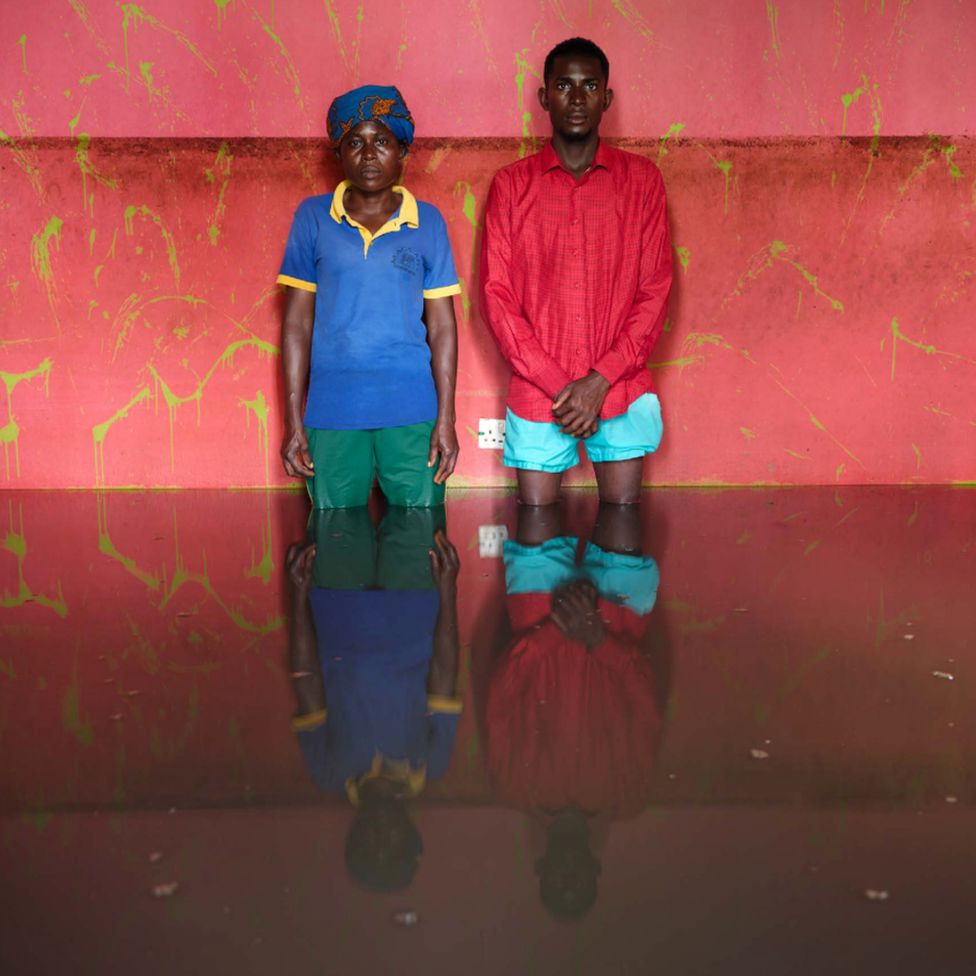 Эдигирару Дональд и Ируаро Роберт стоят в паводковой воде в своем доме в муниципалитете Огбия, штат Байелса, Нигерия, ноябрь 2022 г.