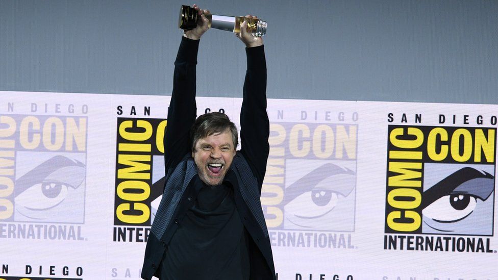 Mark Hamill smiles as he holds up the Icon award at Comic Con
