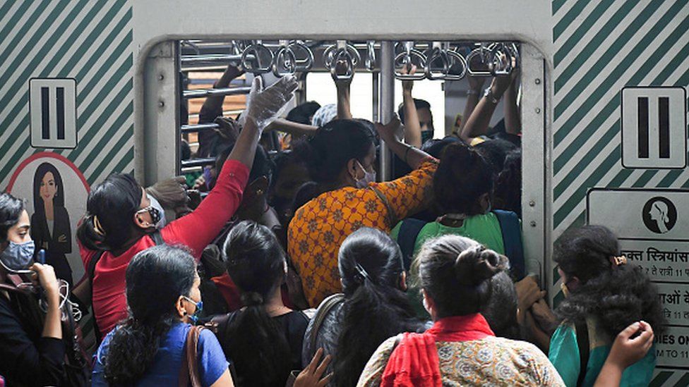 Passengers wearing facemasks are boarding a local train at a railway station in Mumbai.