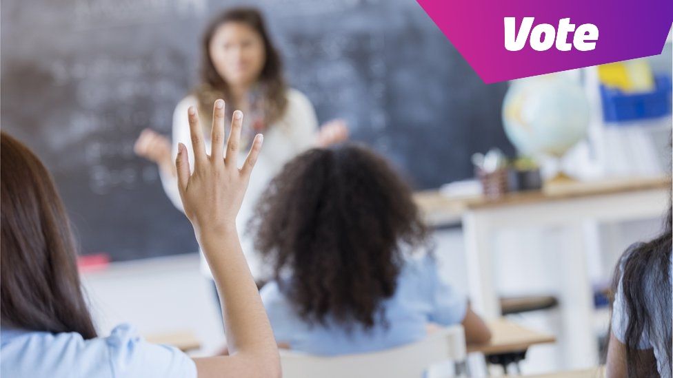 children in classroom with hands raised