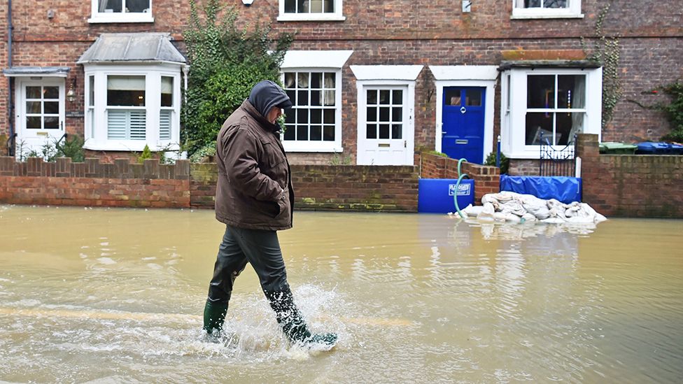 A man walks through flood water, as pumps and flood barriers help to keep the water from flooding homes in Gloucester Road in Tewkesbury, Gloucestershire, following the aftermath of Storm Dennis in Feb 2020