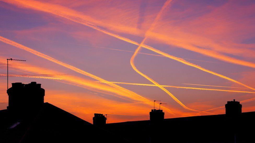 Aeroplane contrails glowing in a sunset over rooftops