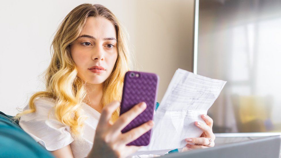 Женщина смотрит на свой телефон и лист бумаги