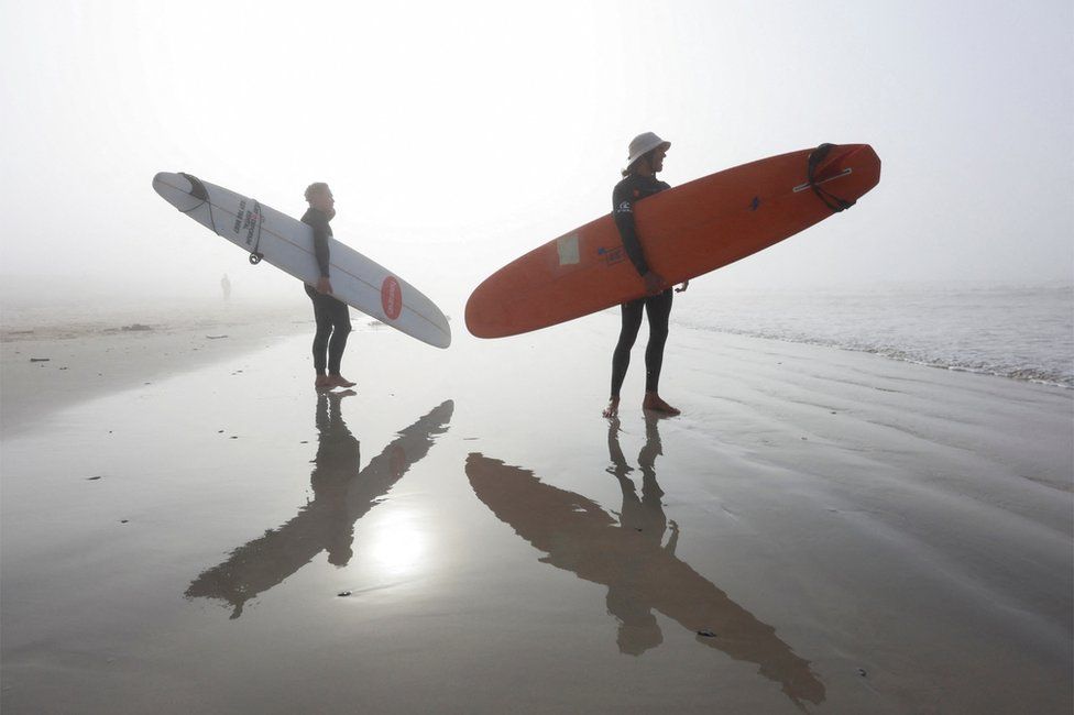 Surfers stand on Surfers stand on Muizenberg beach in the early morning as seasonal mist shrouds the sun in Cape Town.