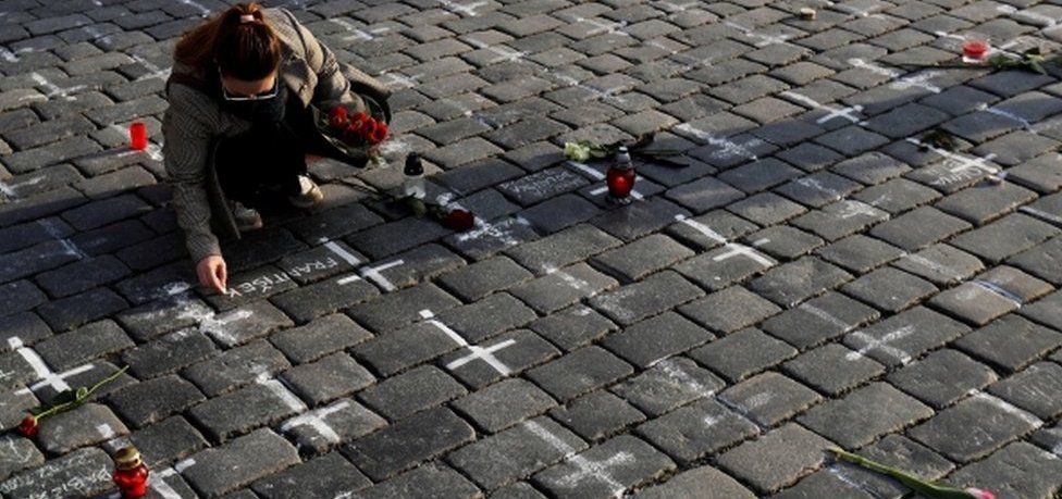 A woman writes a name next to a painted cross to commemorate Czech coronavirus deaths in Prague's Old Town Square