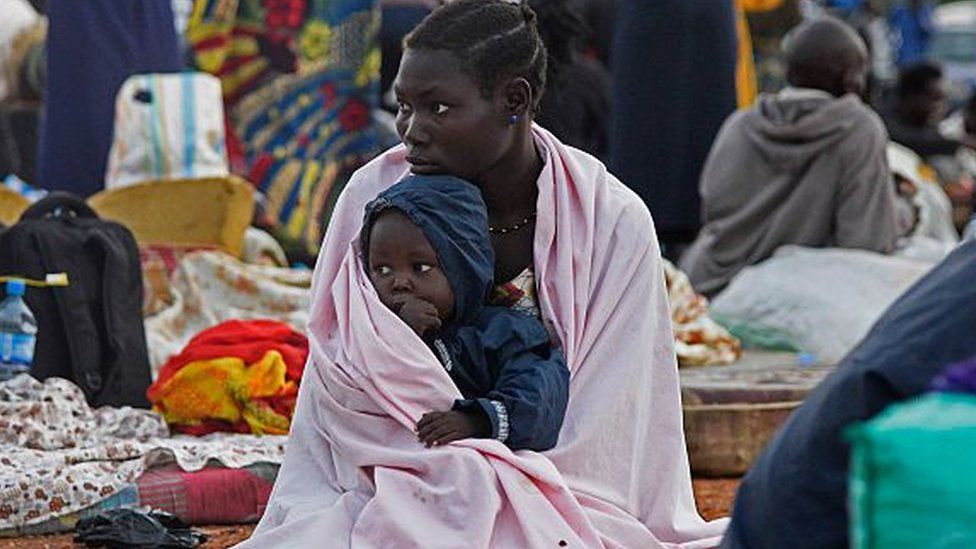A woman from South Sudan holds a child on her knees as she sits inside a make-shift camp at Nimule border, in Amuru Distric in Uganda on 16 July 2016