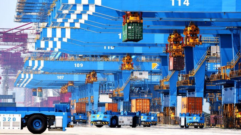 Auto-transporters and cranes move containers on a dockyard of a port in Qingdao in east China