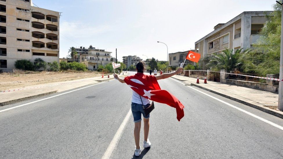 A woman walks while holding Turkish and Turkish Cypriot flags inside an area fenced off by the Turkish military since 1974
