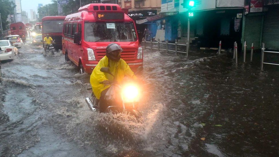 People deal with the water clogging in the wake of Cyclone Tauktae at Dadar TT circle on May 17, 2021 in Mumbai, India.