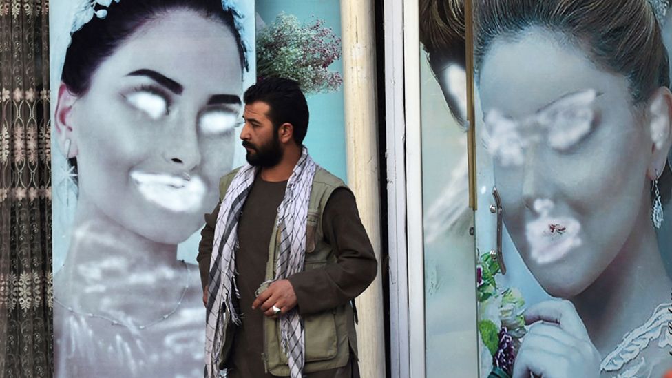 A man stands next to a beauty salon with images of women defaced using spray paint in Kabul