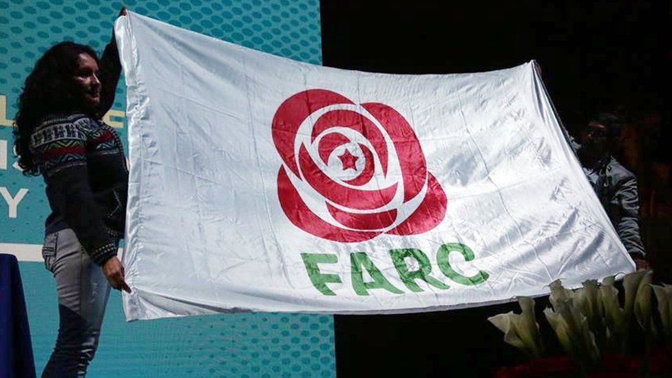 The new logo of the Farc political party, a stylised red rose icon, is displayed on a white flag with the letters FARC, held by two people