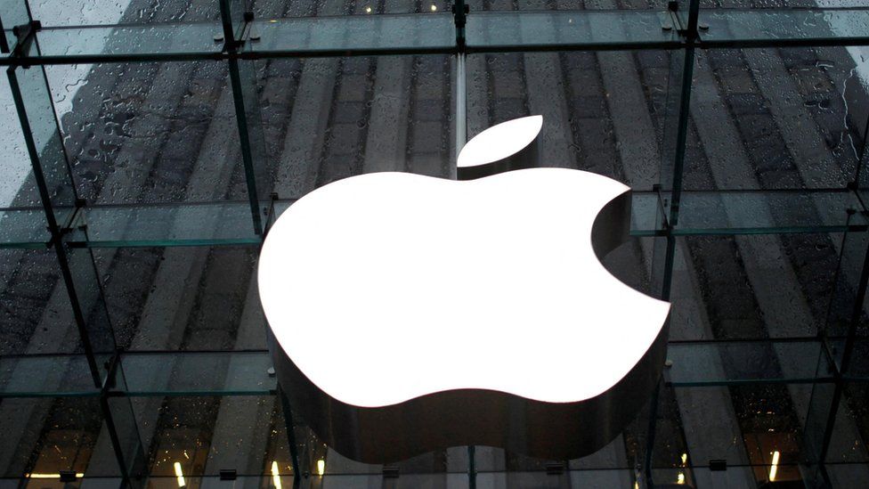 Apple logo in white in front of buildings on rainy day.