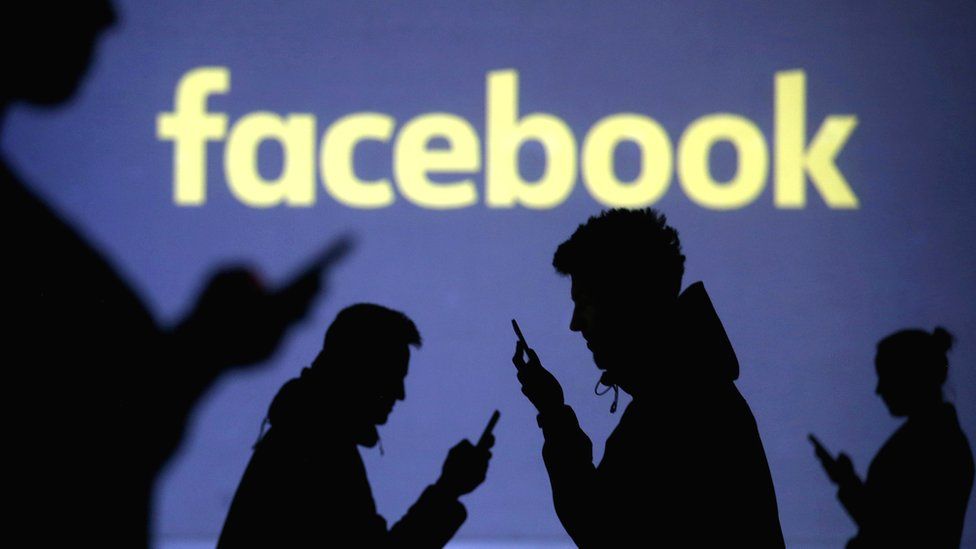 Silhouettes of mobile users next to a screen projection of the Facebook logo, 28 March 2018