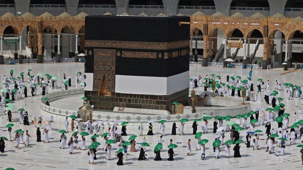 Паломники, держащие умреллы, чтобы защитить себя от жары, прибывают в Каабу, самую священную святыню ислама, в Великую мечеть в священном городе Мекка