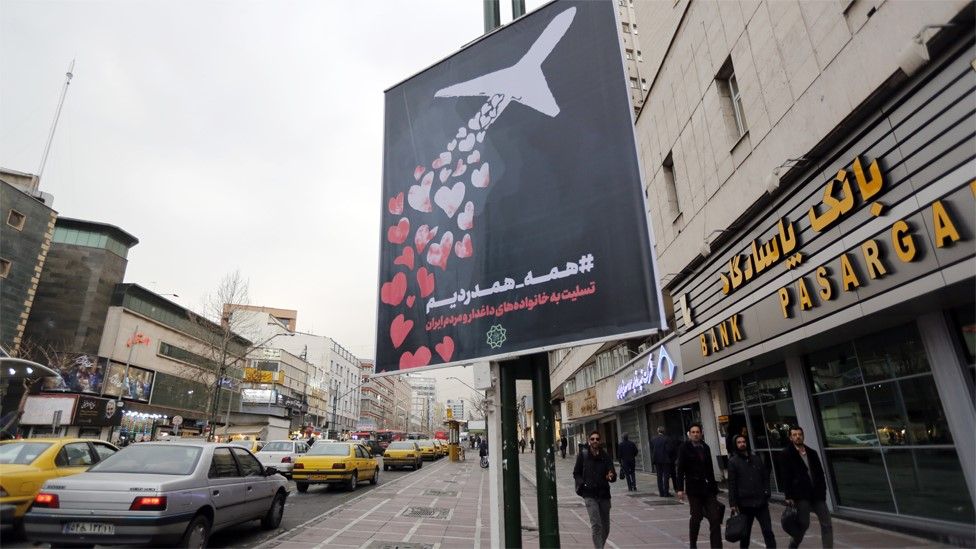 People walk past a banner on a lamppost in Tehran saying: "We are all in pain and sympathise"