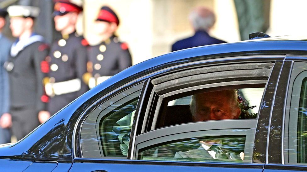 King Charles smiles and looks out through a window of the car taking him to St Anne's Cathedral in Belfast