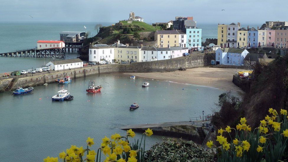 Tenby harbour, with fishing boats in the sea, and houses and a slipway in the distance