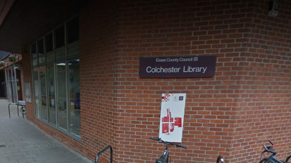 A brick wall exterior with a brown sign reading Colchester Library.