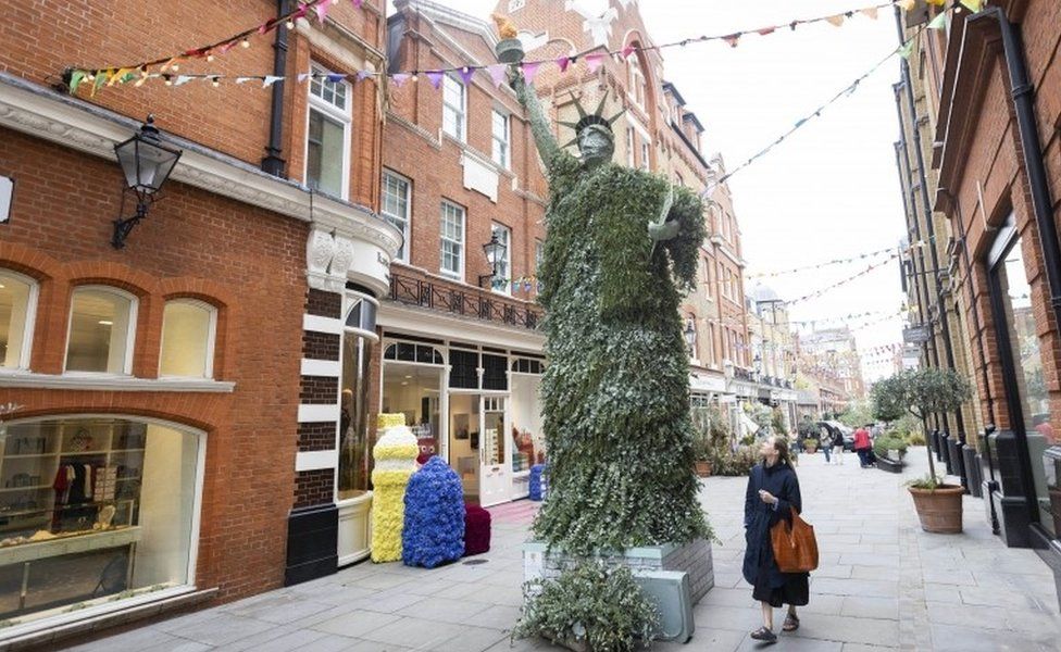 Sophie Danks passes by a Statue of Liberty design from the "Extraordinary Voyages" themed floral installations as it goes on display at Pavilion Road as part of this year"s Chelsea in Bloom,