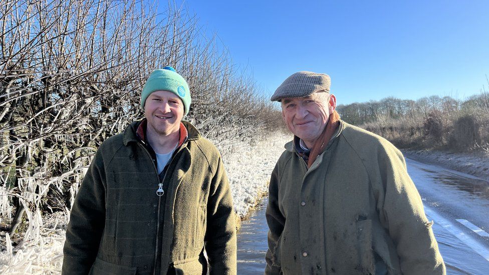 Two men stood on a road with icy hedges