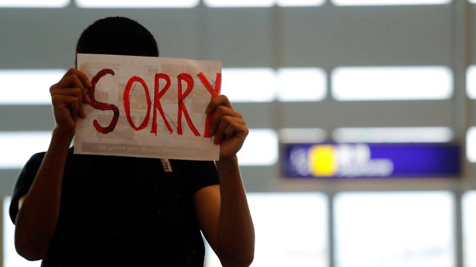 An anti-extradition bill protester offers an apology to passengers blocked from entering the security gates during a mass demonstration after a woman was shot in the eye, at the Hong Kong international airport