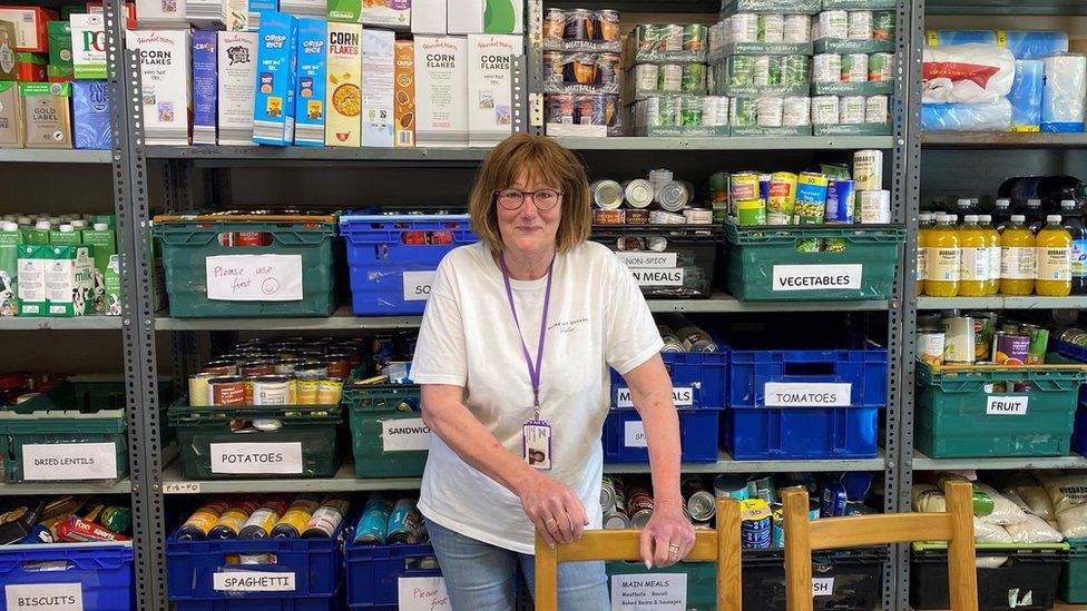 Broke Not Broken stock controller Susan in front of a large shelf full of different types of food