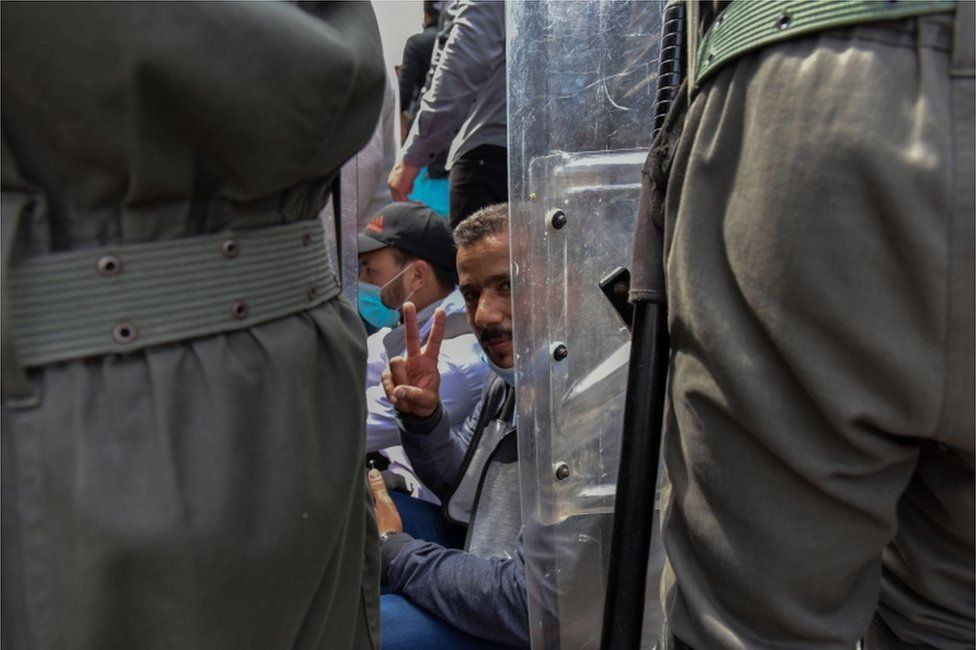 A detained protester gestures as security forces disperse a demonstration.