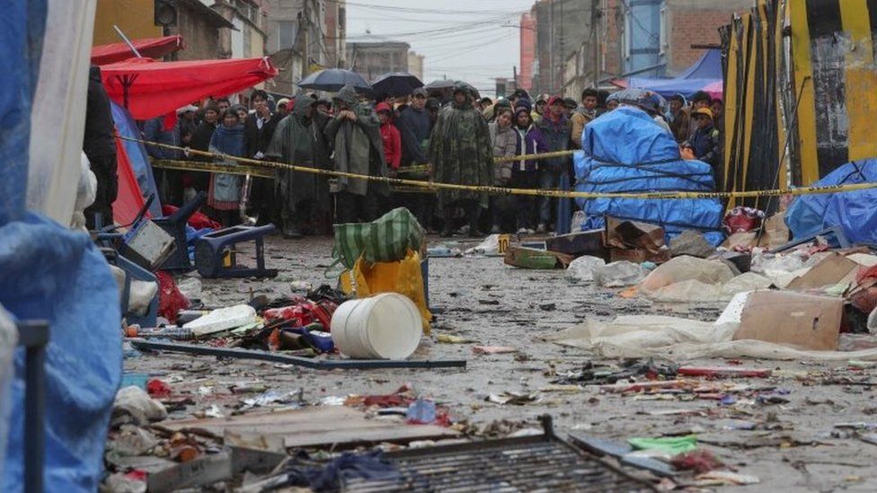 Locals watch from behind of a barricade at the scene of an explosion a day before, that caused six dead and 28 injured in a street market that remains cordoned off while the investigation continues in the city of Oruro, Bolivia,