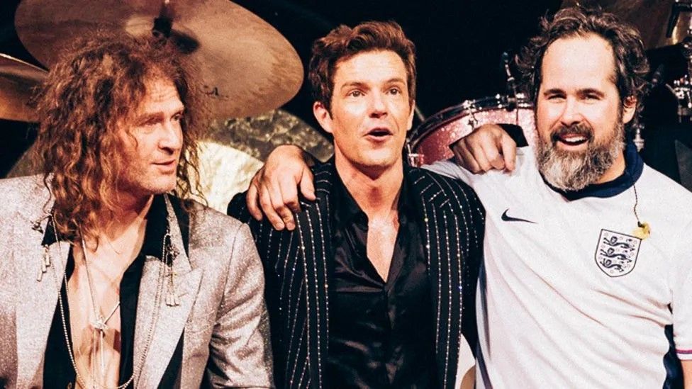 The Killers stand together at the end of their gig, with drummer Ronnie Vannucci Jr wearing an England football shirt