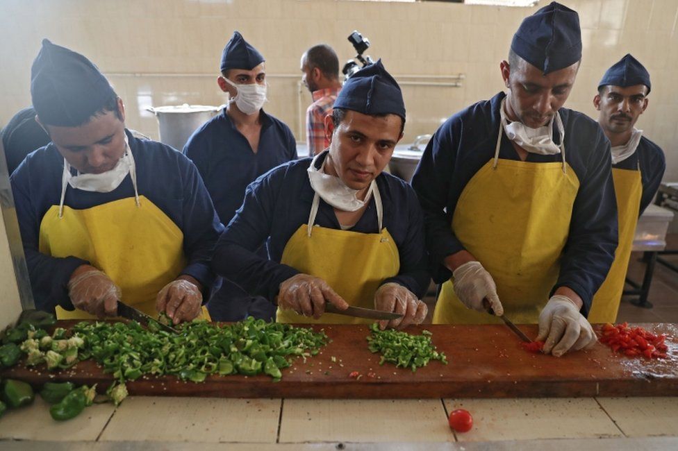 Prison inmates chop vegetables in a kitchen