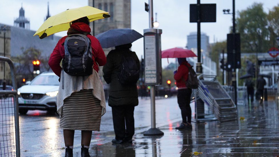 People hold umbrellas as they wait in the rain at a bus stop in Whitehall, London on Thursday