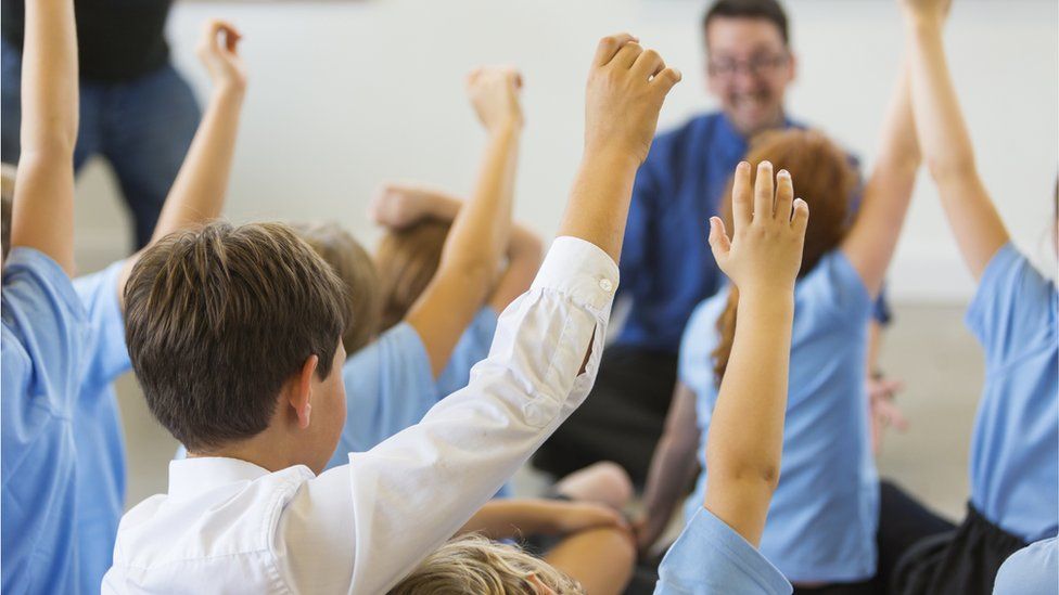 Children raise hands in class to male teacher