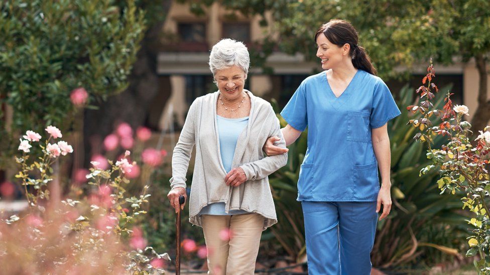 A nurse and a woman with a walking stick in an outdoor space