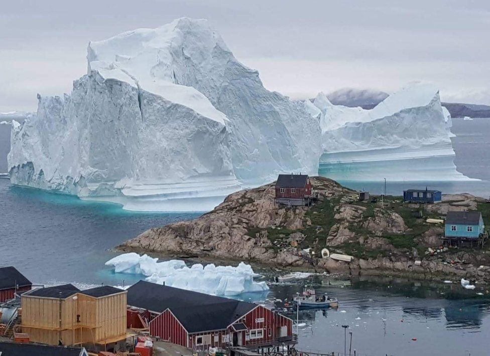 A giant iceberg is seen behind an Innaarsuit settlement, Greenland