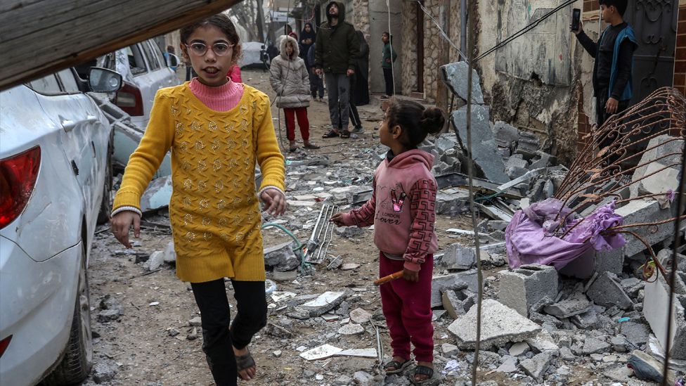 Palestinian children walk among the damaged cars and apartment building belonging to the al-Mashuhi family, part of which collapsed, after Israeli attacks in Rafah, Gaza on 9 February 2024