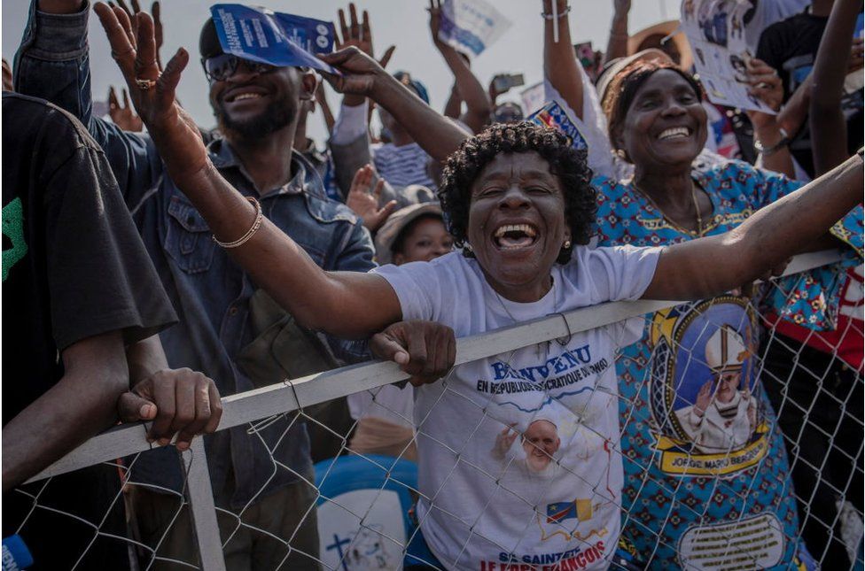 Crowd cheering in DR Congo, wearing t-shirts with the Pope's face on it.