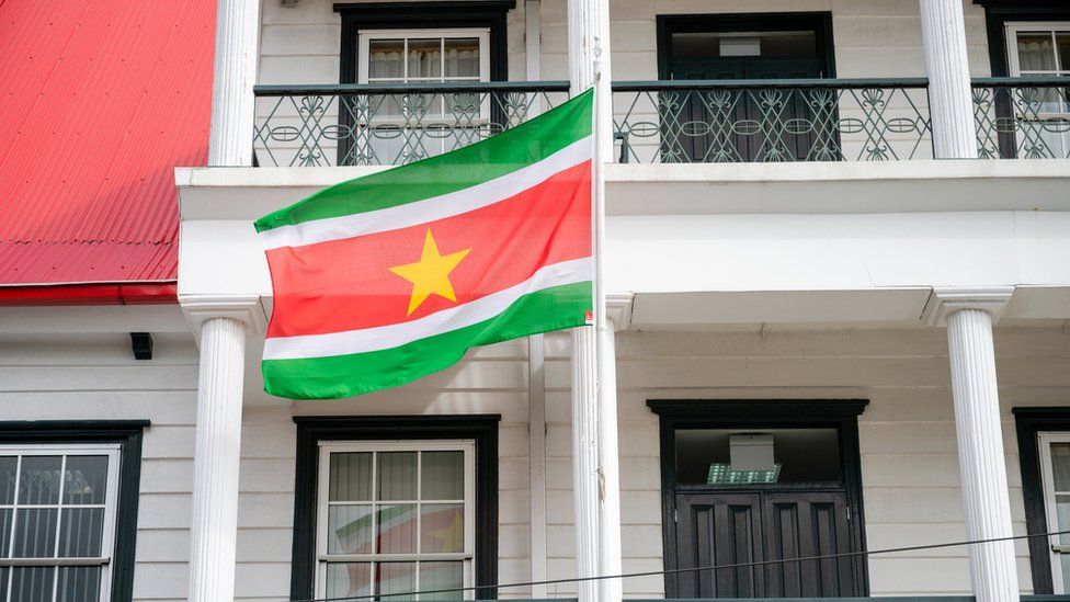 National flag of Suriname flying in front of a Dutch-colonial style building in the capital Paramaribo