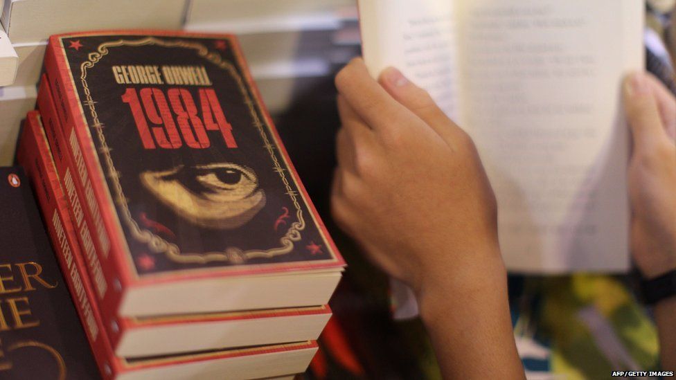Someone's hands holding a book next to copies of 1984