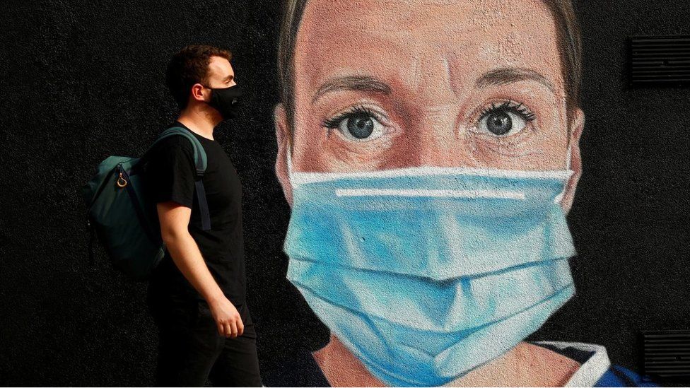 A man wearing a protective face mask walks by a mural of a medical worker in Manchester city centre