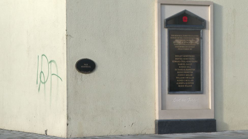 Letters IRA painted on a wall next to a memorial to victims of an IRA bomb