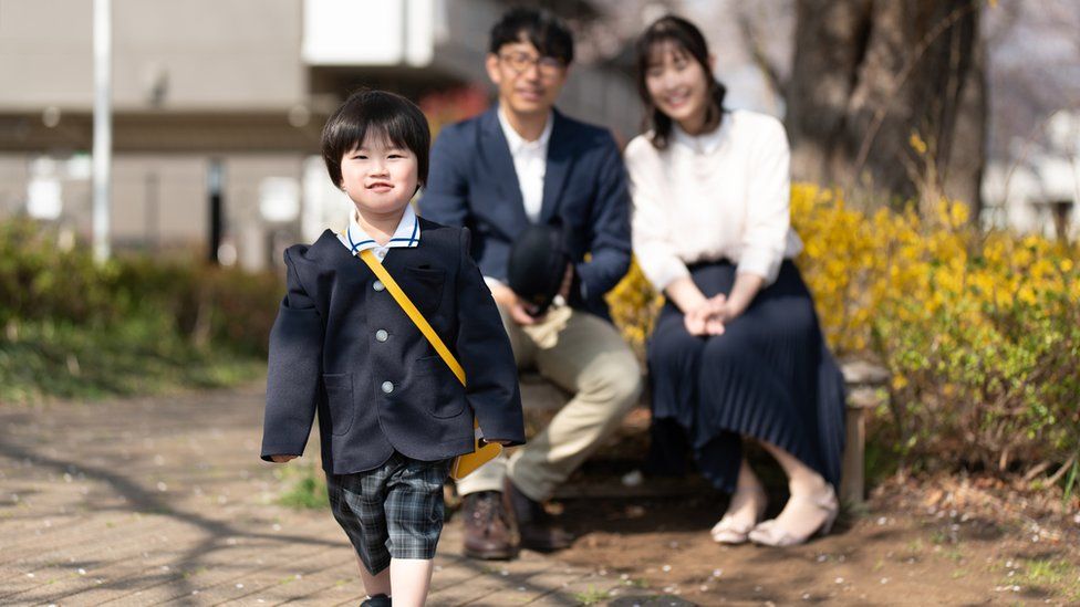 Uma menina japonesa vai para a escola enquanto seus pais a observam