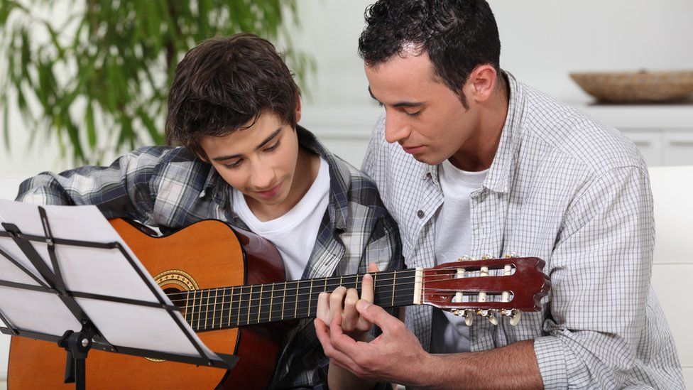 A Bark guitar teacher helping a boy to learn the instrument