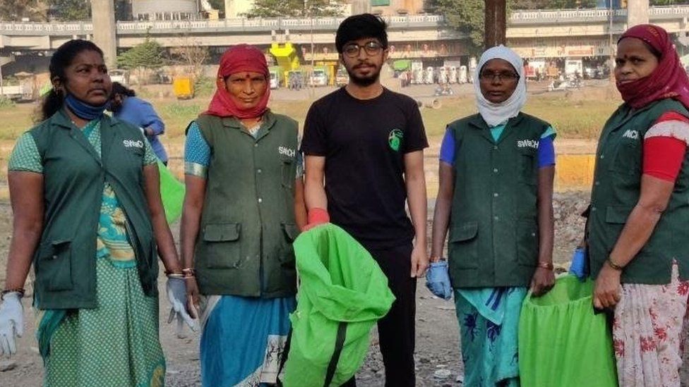Five volunteers; four women and one man, holding green bags to collect rubbish in India