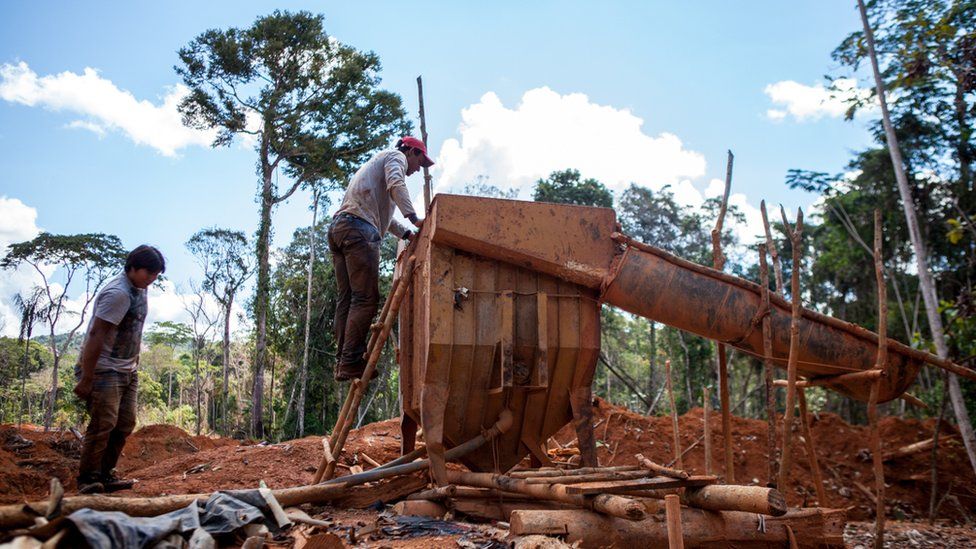 Two men are working a machine in a deforested area