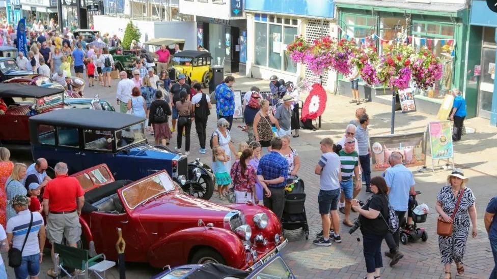 Dozens of people line a high street in Gloucester as they look at classic cars