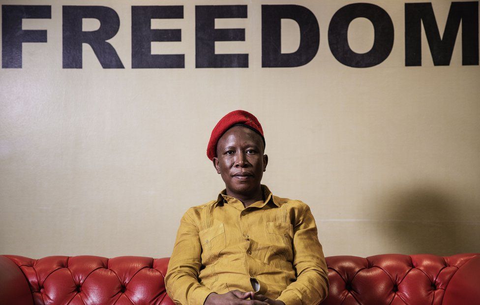 Julius Malema sits in front of a sign that says Freedom