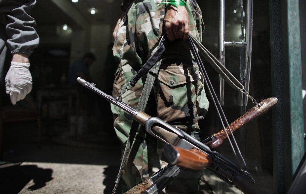 A Syrian rebel holds AK-47 rifles belonging to wounded comrades