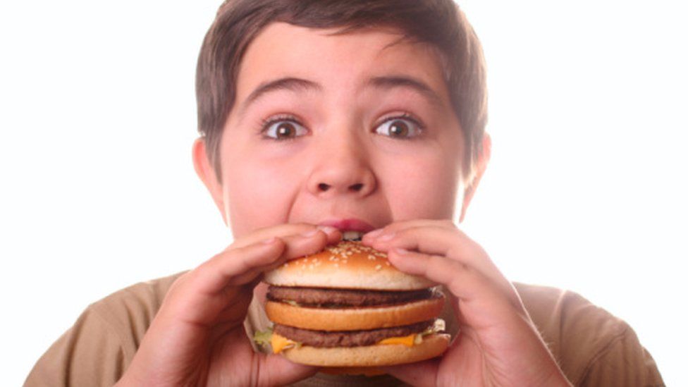 Overweight boy tucking into a burger