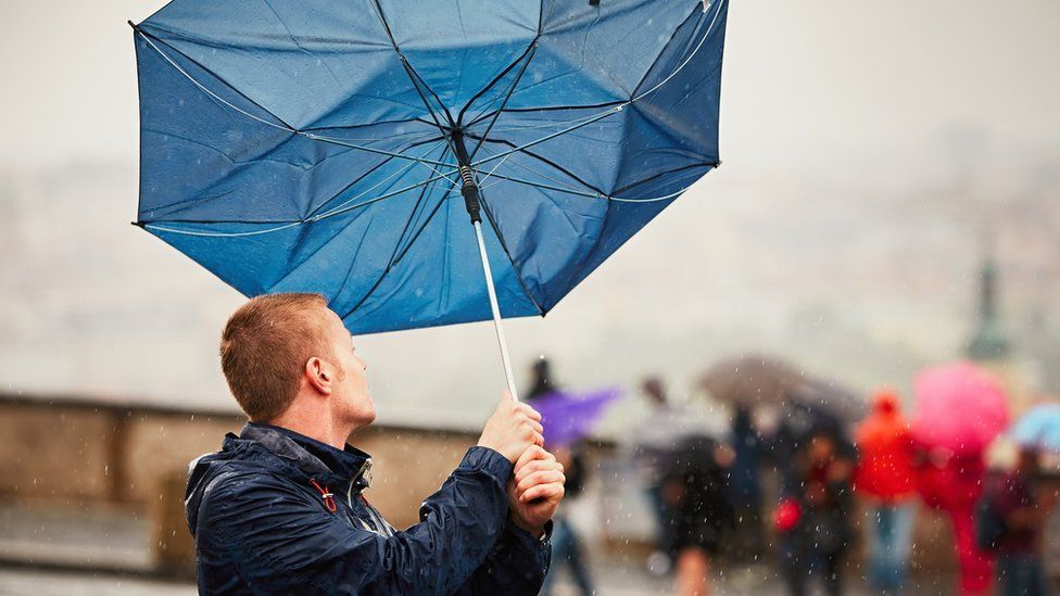 A man holds an umbrella which has blown inside out